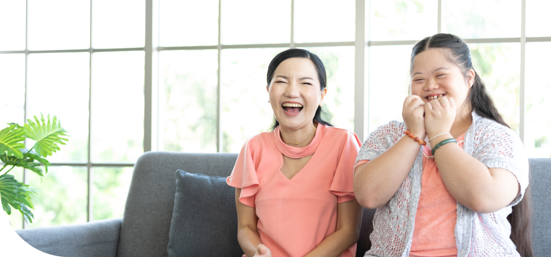 A woman and a young girl sitting on a sofa and laughing together.
