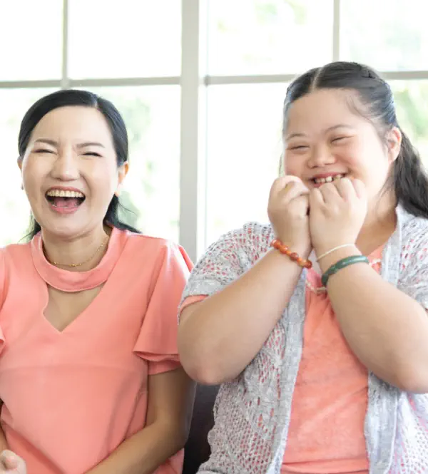 A woman and a young girl sitting on a sofa and laughing together.