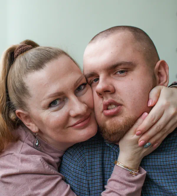 A woman leaning her face lovingly against a young man wearing a blue shirt