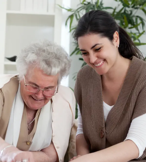 A young caregiver or family member smiling while spending time with an elderly woman