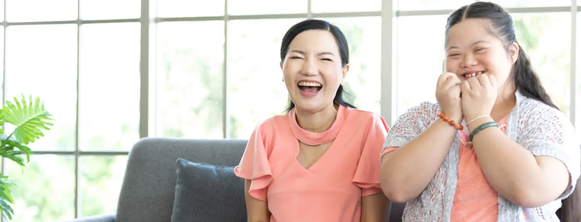 A woman and a young girl sitting on a sofa and laughing together.