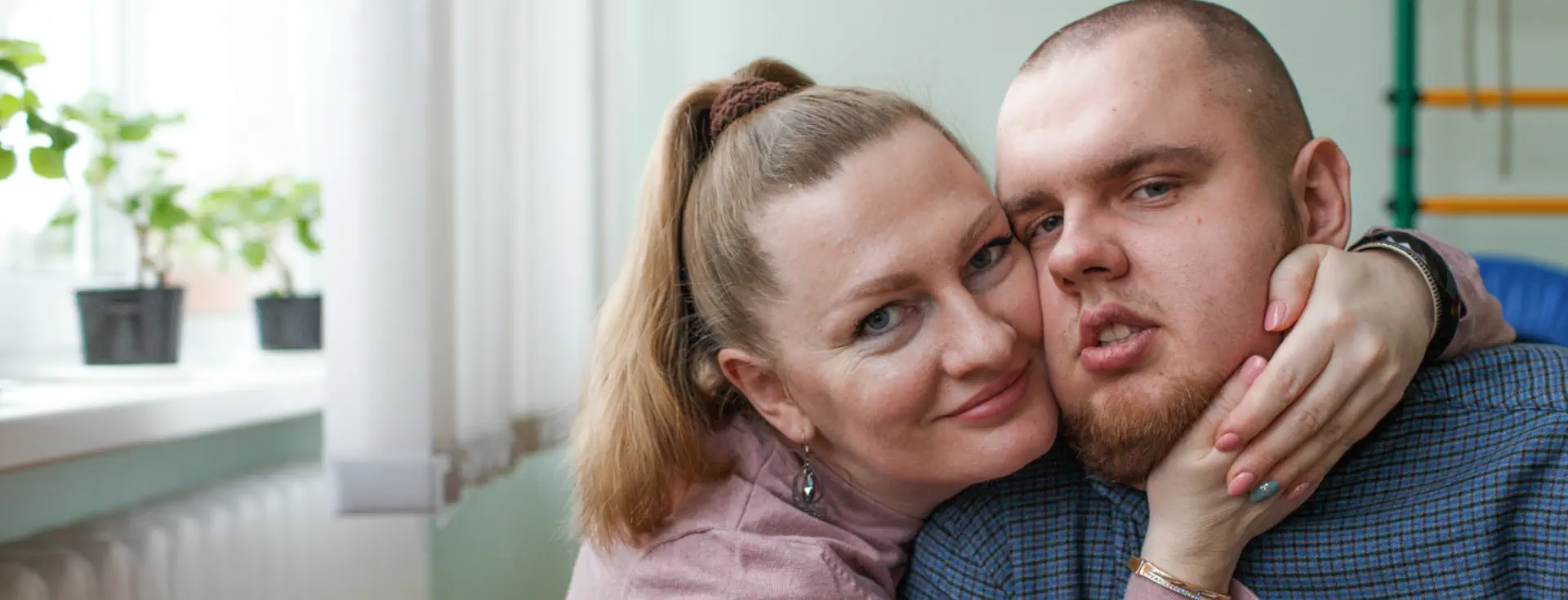A woman leaning her face lovingly against a young man wearing a blue shirt