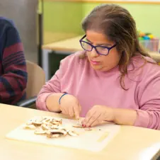 woman wearing glasses and a pink sweater focused on writing