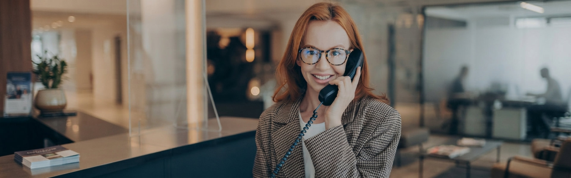 Smiling Professional Woman Talking on Landline Phone in Modern Office
